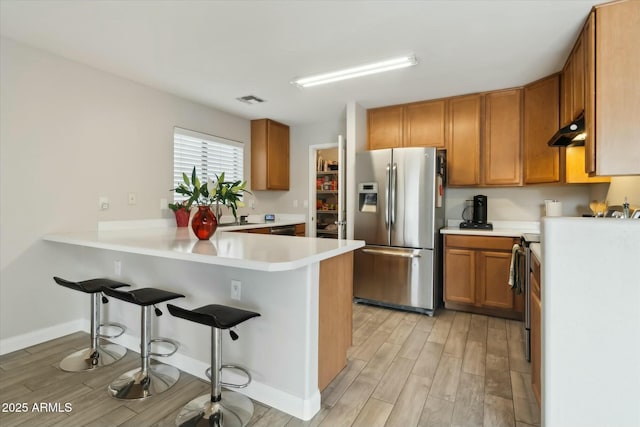 kitchen featuring a peninsula, light countertops, a kitchen bar, brown cabinetry, and stainless steel fridge