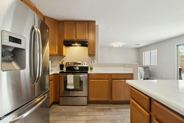 kitchen featuring brown cabinets, wood tiled floor, stainless steel appliances, light countertops, and under cabinet range hood