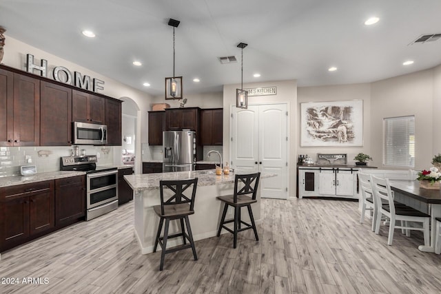 kitchen with light stone countertops, a center island with sink, stainless steel appliances, and light wood-type flooring