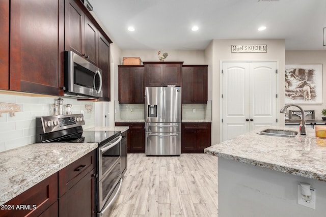 kitchen featuring light stone countertops, appliances with stainless steel finishes, decorative backsplash, sink, and light hardwood / wood-style flooring