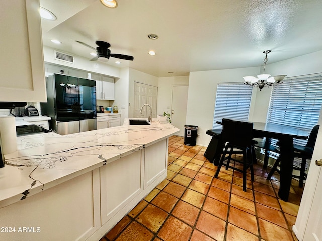 kitchen featuring sink, ceiling fan with notable chandelier, white cabinets, decorative light fixtures, and stainless steel fridge