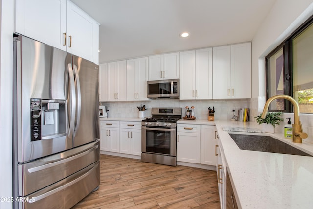 kitchen featuring appliances with stainless steel finishes, light wood-type flooring, white cabinets, and a sink