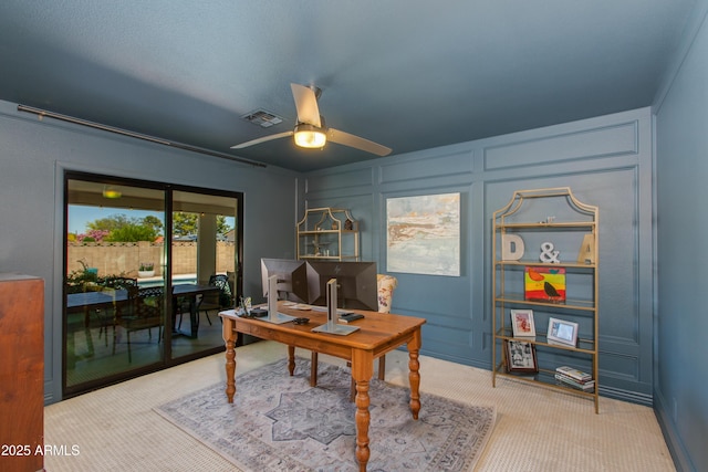 office space with a ceiling fan, visible vents, a decorative wall, and carpet floors