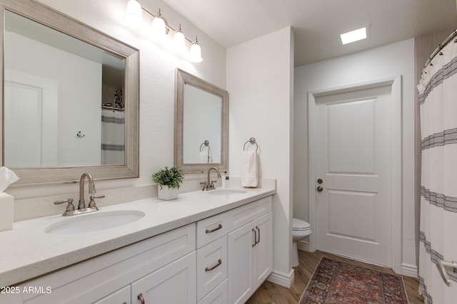 full bathroom featuring toilet, double vanity, a sink, and wood finished floors