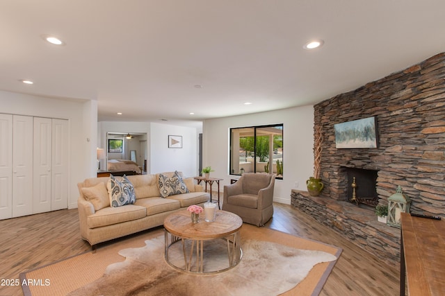 living area featuring recessed lighting, a stone fireplace, and wood finished floors