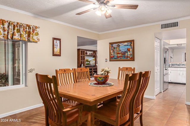 dining space with ceiling fan, a textured ceiling, crown molding, and light tile patterned flooring