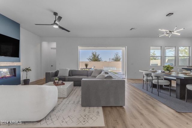 living room with ceiling fan with notable chandelier and light hardwood / wood-style flooring