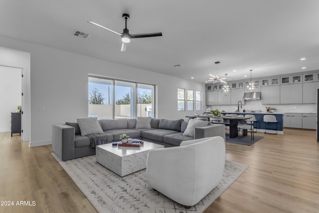 living room featuring ceiling fan with notable chandelier, light hardwood / wood-style flooring, and sink