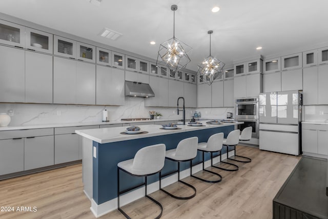 kitchen featuring appliances with stainless steel finishes, hanging light fixtures, light hardwood / wood-style floors, an island with sink, and a chandelier