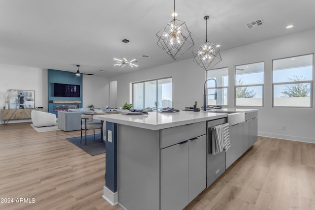 kitchen with ceiling fan with notable chandelier, gray cabinets, light wood-type flooring, decorative light fixtures, and a kitchen island with sink