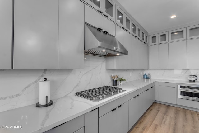 kitchen with light stone countertops, appliances with stainless steel finishes, tasteful backsplash, and light hardwood / wood-style flooring