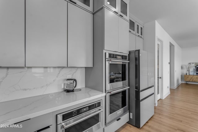 kitchen with appliances with stainless steel finishes, white cabinetry, tasteful backsplash, light stone countertops, and light wood-type flooring