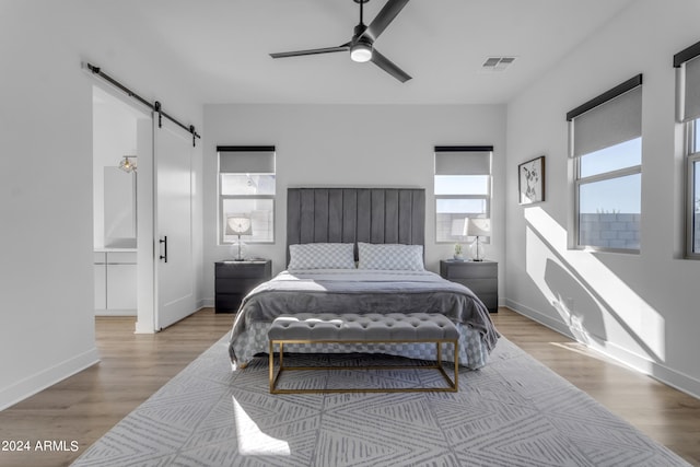 bedroom with light wood-type flooring, ceiling fan, and a barn door