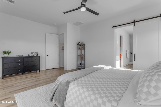 bedroom featuring a barn door, ceiling fan, and light hardwood / wood-style flooring