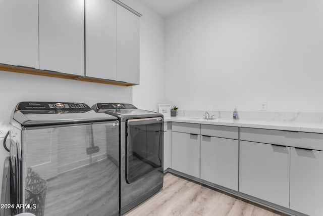 clothes washing area featuring cabinets, light wood-type flooring, sink, and washing machine and clothes dryer