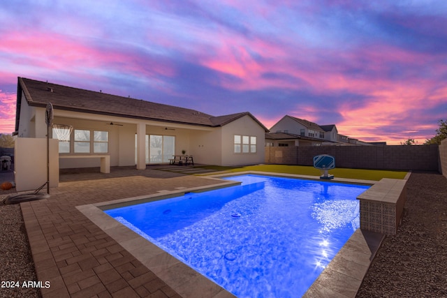 pool at dusk featuring ceiling fan and a patio area