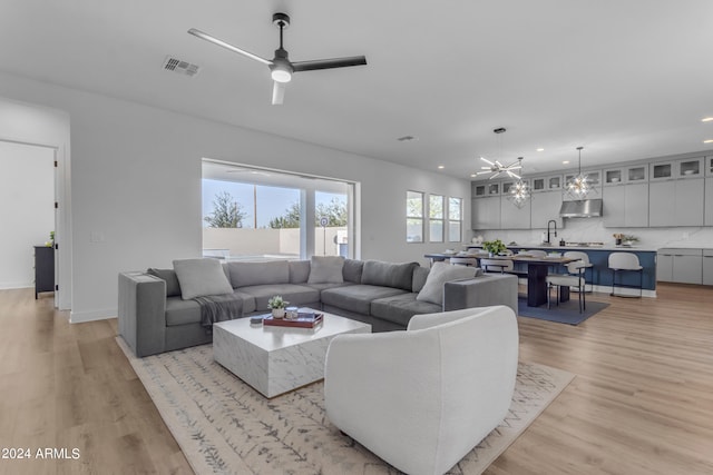 living room featuring ceiling fan with notable chandelier, light wood-type flooring, and sink