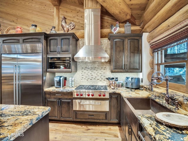 kitchen with sink, wall chimney exhaust hood, stainless steel built in refrigerator, dark brown cabinets, and light wood-type flooring