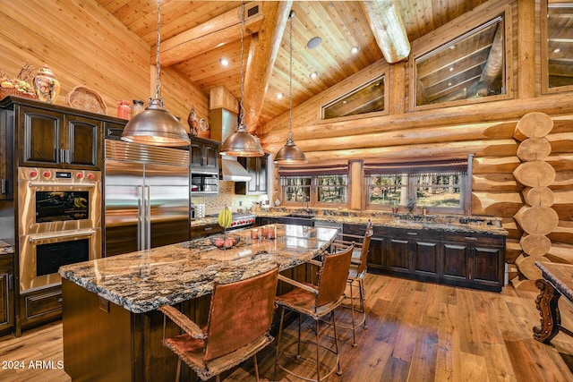 kitchen with appliances with stainless steel finishes, light wood-type flooring, dark stone counters, dark brown cabinets, and a large island