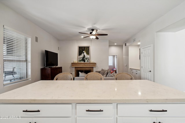 kitchen with white cabinetry, light stone countertops, and ceiling fan