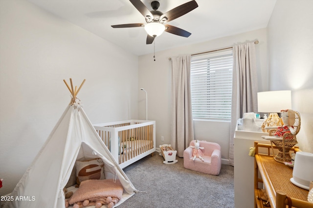 bedroom featuring a nursery area, carpet flooring, and ceiling fan