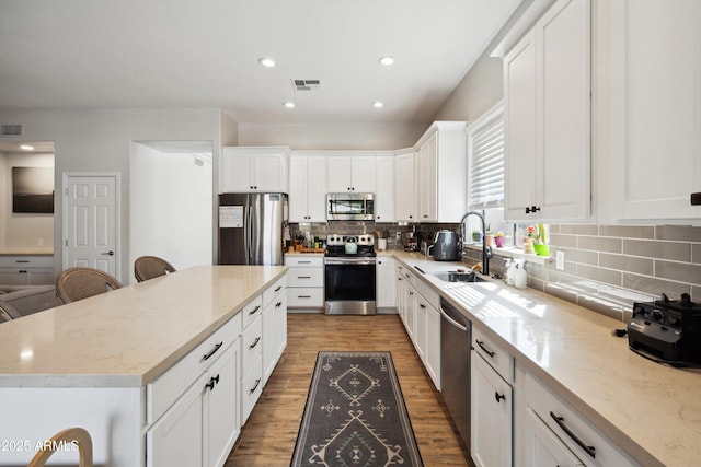 kitchen with a breakfast bar, sink, white cabinetry, appliances with stainless steel finishes, and a kitchen island