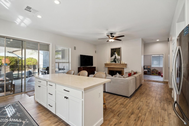 kitchen featuring a breakfast bar area, white cabinetry, stainless steel fridge, a kitchen island, and light hardwood / wood-style floors