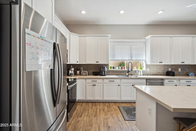 kitchen with sink, white cabinetry, light wood-type flooring, appliances with stainless steel finishes, and backsplash