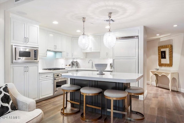 kitchen featuring a breakfast bar area, pendant lighting, light hardwood / wood-style flooring, stainless steel appliances, and white cabinets