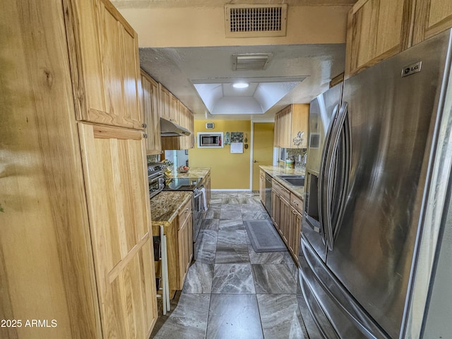 kitchen with appliances with stainless steel finishes, under cabinet range hood, a tray ceiling, baseboards, and light countertops