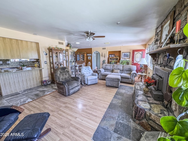 living room featuring ceiling fan, a fireplace, and wood finished floors