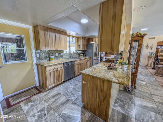 kitchen featuring stainless steel appliances, a tray ceiling, a sink, light stone countertops, and a peninsula