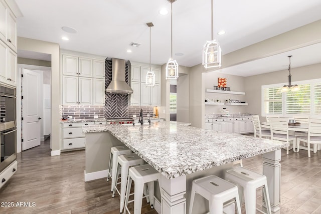 kitchen with a large island, wall chimney range hood, hanging light fixtures, and a breakfast bar