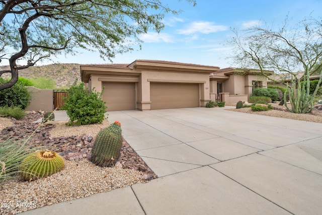 prairie-style house with stucco siding, driveway, fence, an attached garage, and a tiled roof