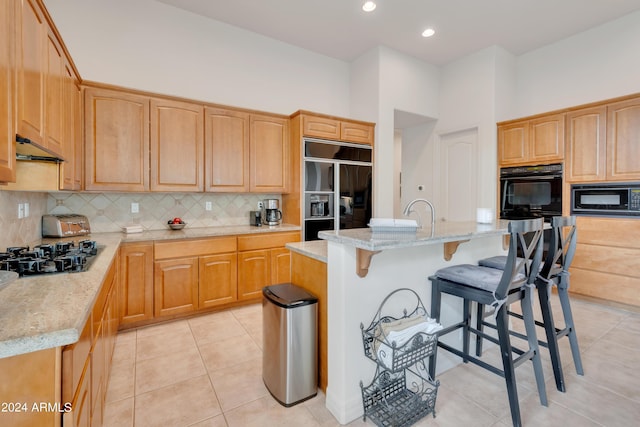 kitchen with backsplash, light stone countertops, a breakfast bar area, light tile patterned floors, and black appliances