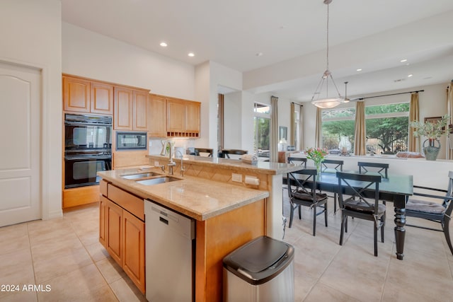 kitchen with decorative light fixtures, light stone countertops, sink, black appliances, and an island with sink