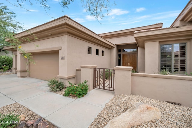 property entrance featuring fence, stucco siding, a garage, driveway, and a gate