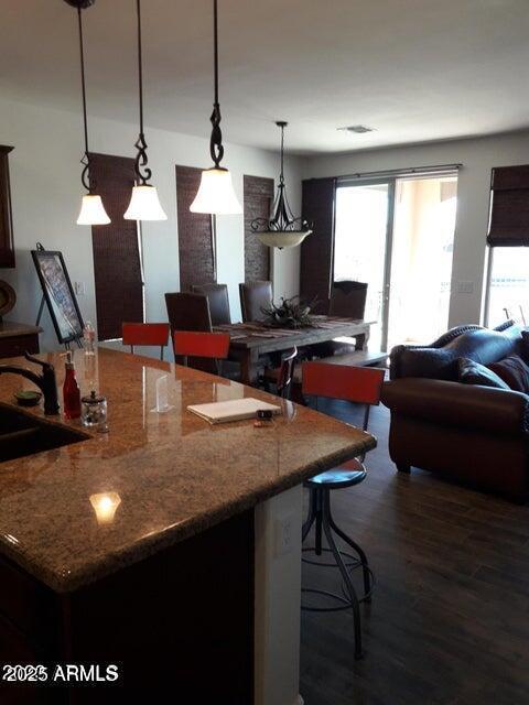 kitchen with a sink, a kitchen breakfast bar, open floor plan, dark wood-style floors, and decorative light fixtures