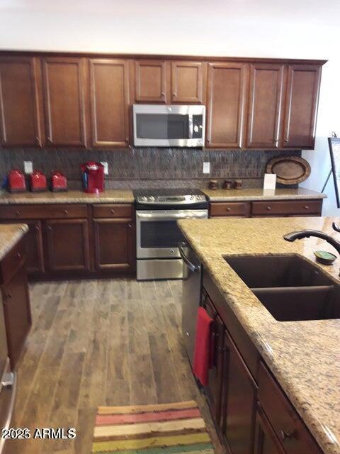 kitchen with stainless steel appliances, a sink, light wood-style flooring, and decorative backsplash