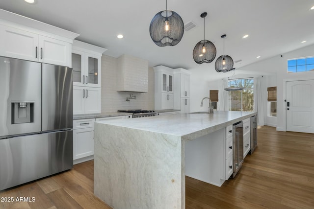 kitchen with an island with sink, stainless steel fridge, glass insert cabinets, and white cabinetry