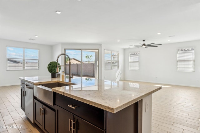 kitchen with light stone counters, a center island with sink, stainless steel dishwasher, open floor plan, and a sink