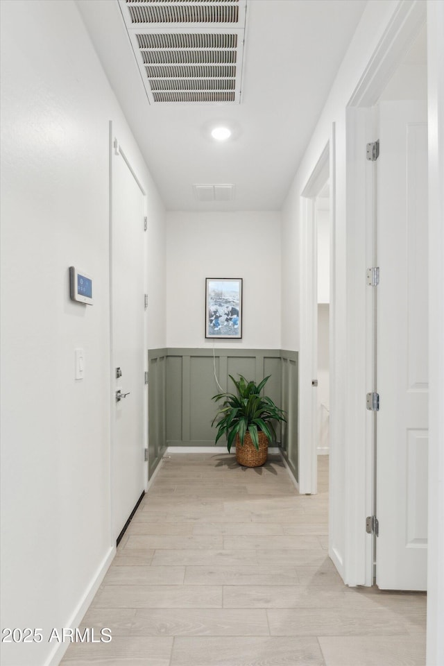 hall with light wood-type flooring, a wainscoted wall, visible vents, and a decorative wall