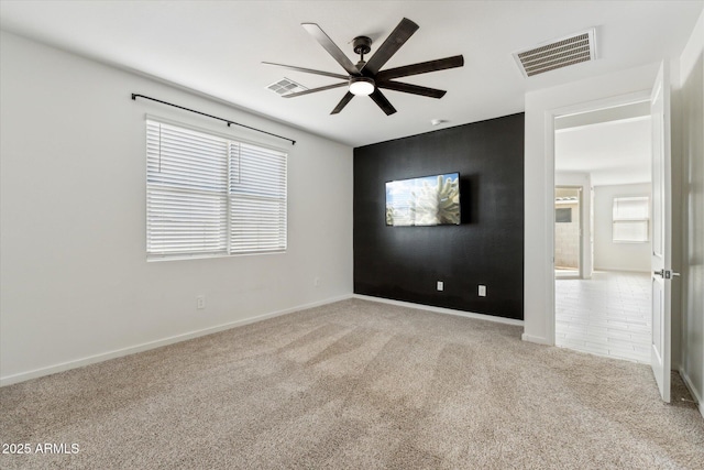 carpeted empty room featuring baseboards, visible vents, and a ceiling fan