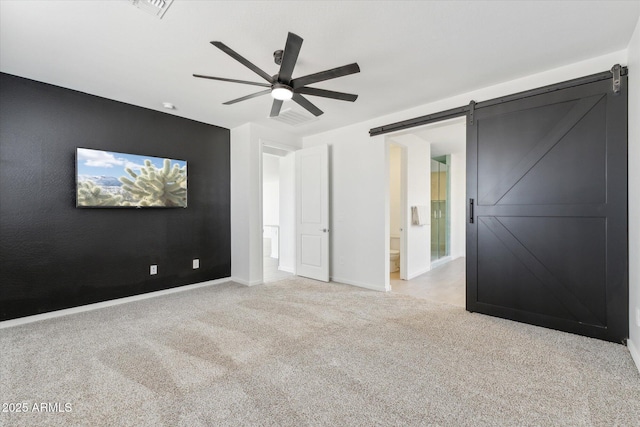 empty room featuring baseboards, a barn door, a ceiling fan, and light colored carpet