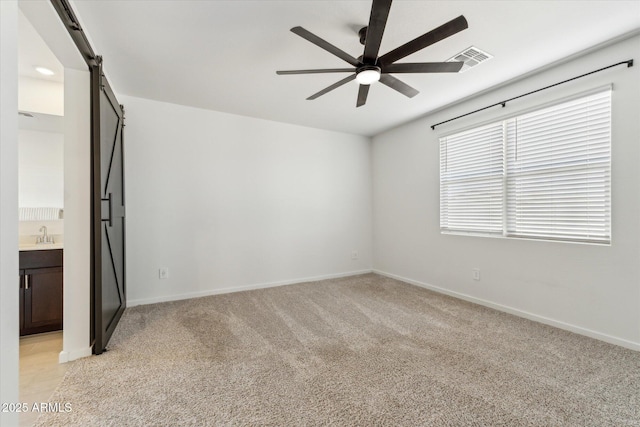 empty room with a ceiling fan, light colored carpet, baseboards, and a barn door