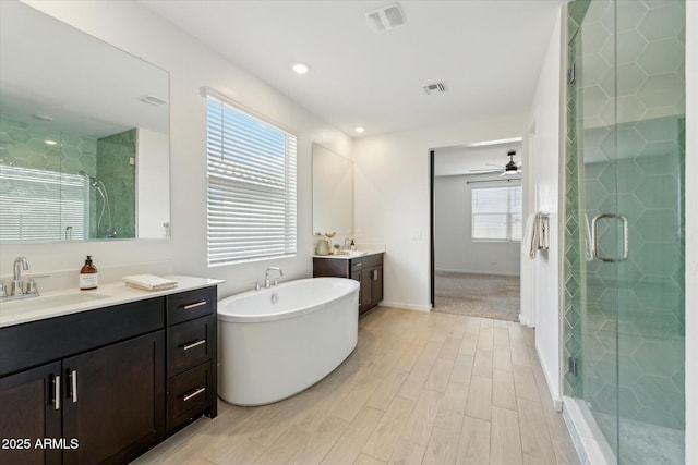 bathroom featuring two vanities, visible vents, a sink, a shower stall, and wood finished floors