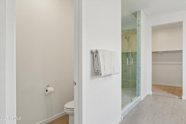 full bath featuring a stall shower, wood finished floors, toilet, and baseboards