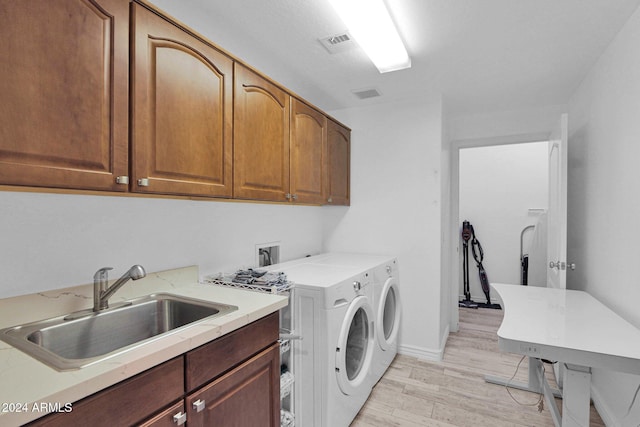 clothes washing area with washer and dryer, cabinet space, visible vents, a sink, and light wood-type flooring