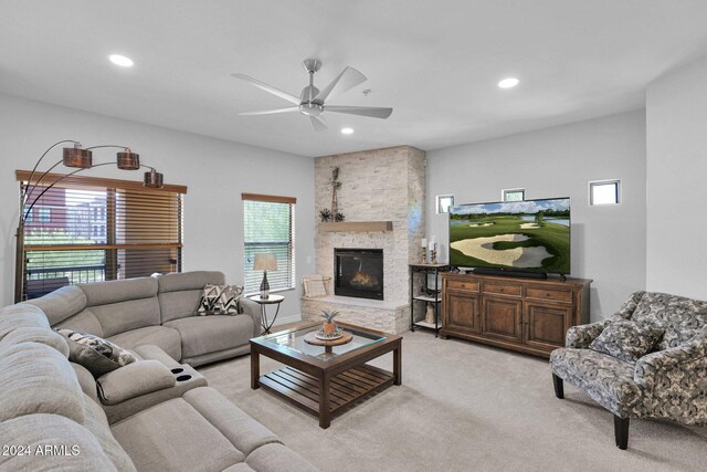 living room with ceiling fan, a stone fireplace, and light carpet