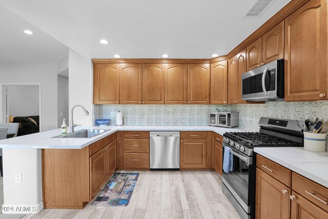 kitchen featuring stainless steel appliances, tasteful backsplash, a sink, light wood-type flooring, and a peninsula